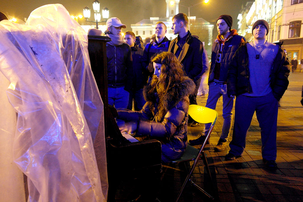 A young lady plays piano, young men are listening
